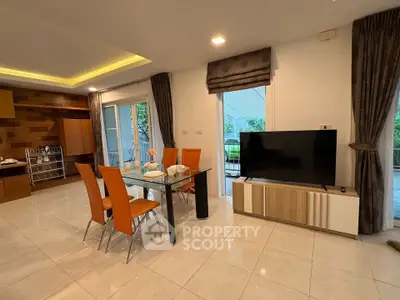 Spacious modern living room with dining area and large TV, featuring elegant decor and natural light.