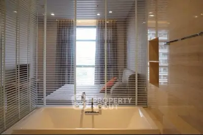 Modern bathroom with bathtub and view into bedroom through glass partition.