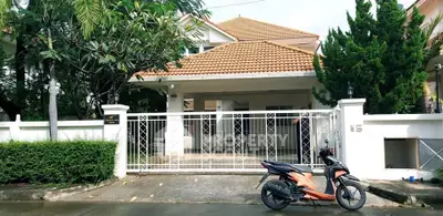 Charming suburban house with tiled roof and gated entrance, featuring lush greenery and a parked scooter.