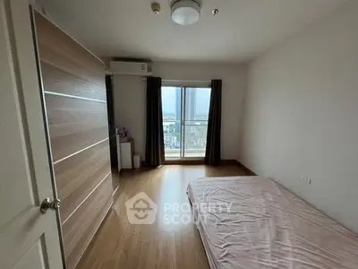 Spacious bedroom with large window and wooden flooring, offering a serene city view.