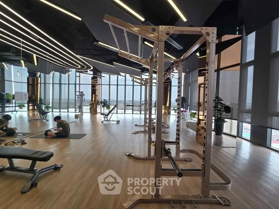 Spacious modern gym with floor-to-ceiling windows and sleek equipment, offering a panoramic city view.
