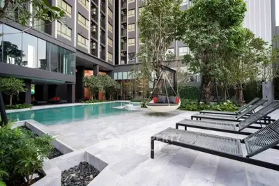 Luxurious modern apartment pool area with stylish lounge chairs and lush greenery.