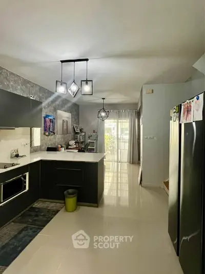 Modern kitchen with sleek black cabinets and open layout, featuring contemporary lighting and a spacious design.