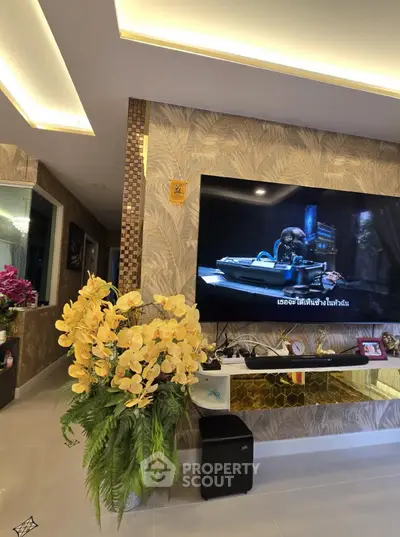 Luxurious living room with modern decor and large TV, featuring elegant lighting and floral arrangement.