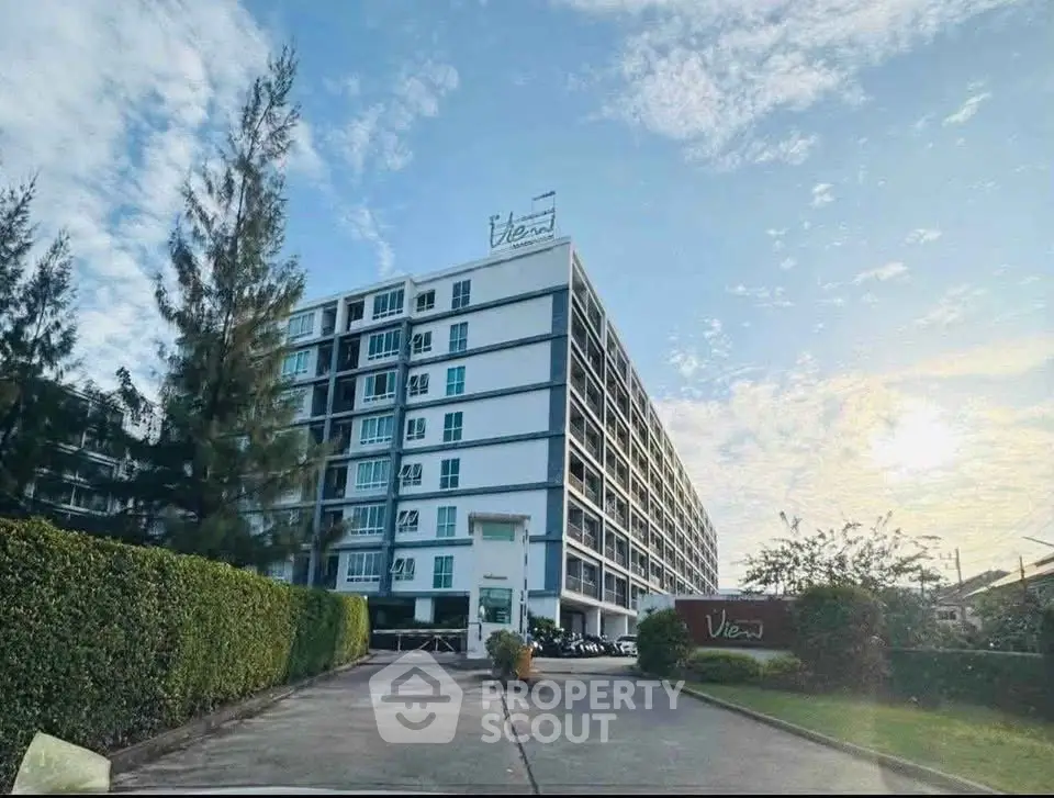 Modern multi-story apartment building with lush greenery and clear blue sky.