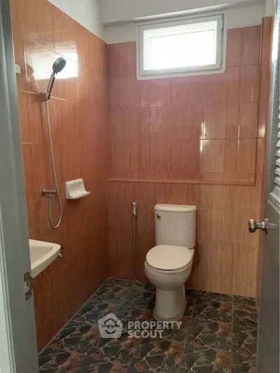 Compact bathroom with tiled walls and floor, featuring a toilet and shower area.