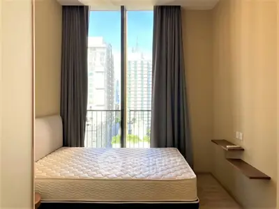 Modern bedroom with large window and city view, featuring a comfortable mattress and minimalist decor.