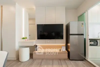 Modern living room with sleek TV setup and stainless steel fridge in stylish apartment.