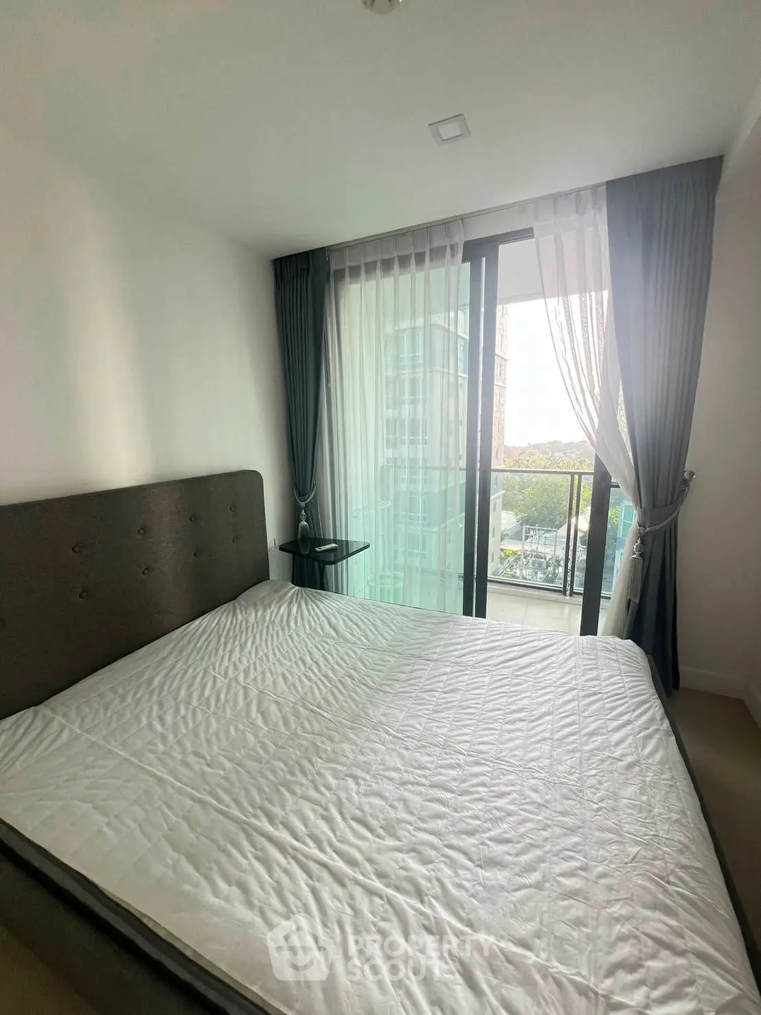 Modern bedroom with large window and city view, featuring elegant curtains and a cozy bed.