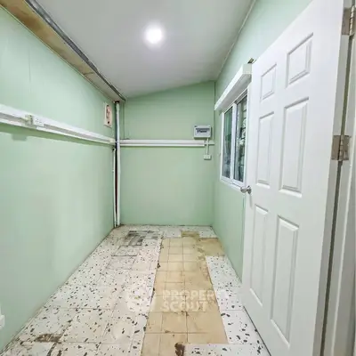Compact storage room with tiled floor and mint green walls, featuring a window and white door.