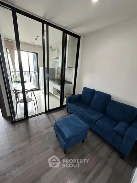 Modern living room with blue sofa and glass partition leading to kitchen
