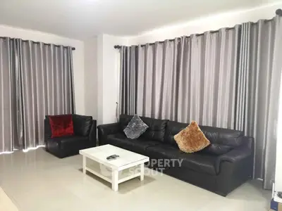Spacious living room with modern black leather sofa and elegant curtains, perfect for relaxation.
