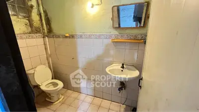 Compact bathroom with tiled walls, small sink, and toilet, ideal for renovation opportunities.