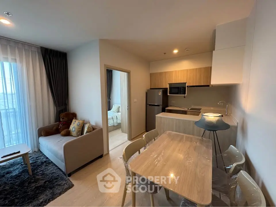 Modern open-plan living room with kitchen and dining area, featuring cozy decor and natural light.