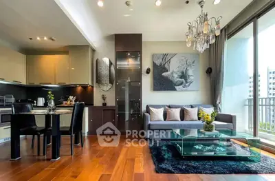 Luxurious modern living room with open kitchen and elegant decor, featuring a glass coffee table and chandelier.