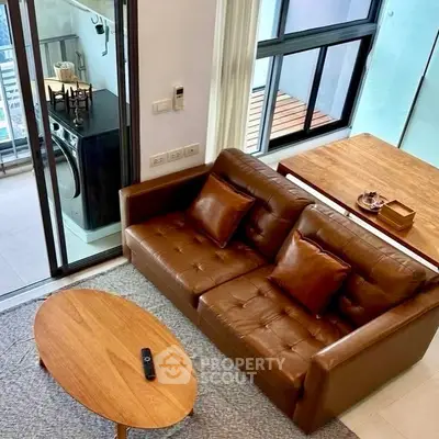 Modern living room with leather sofa and wooden table, featuring a balcony view.