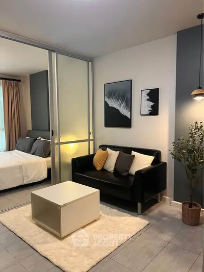 Modern living room with sleek black sofa, stylish decor, and cozy bedroom view in open-plan apartment.