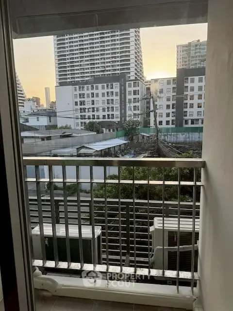 Urban apartment balcony with city view, showcasing modern high-rise buildings at sunset.