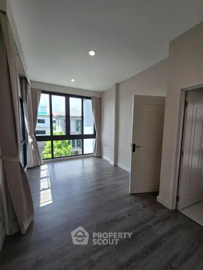 Spacious bedroom with large windows and elegant curtains, offering ample natural light and modern flooring.