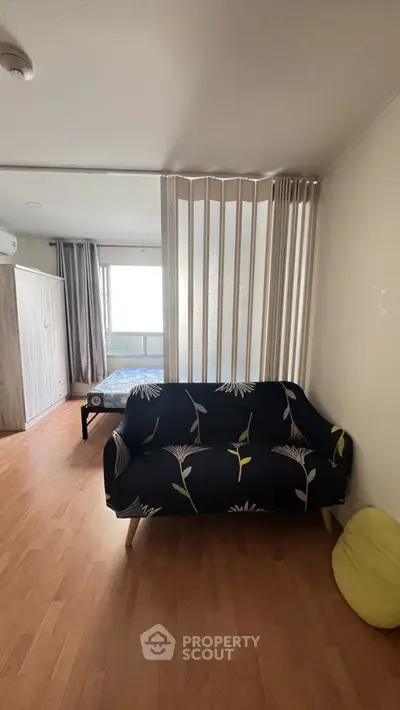 Cozy studio apartment with stylish sofa and partition, featuring natural light and wooden flooring.