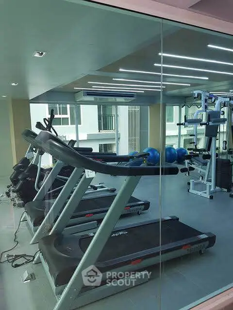 Modern gym with state-of-the-art equipment and large windows in a residential building.