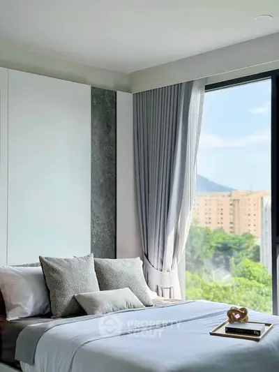 Modern bedroom with large window offering scenic city view, elegant decor, and plush bedding.