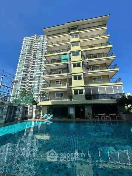 Modern apartment building with pool and spacious balconies under clear blue sky.
