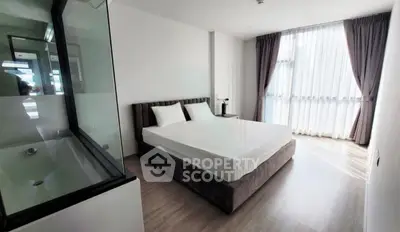 Modern bedroom with large window and glass partition overlooking a bathtub, featuring elegant curtains and sleek flooring.