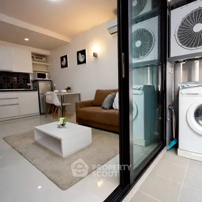 Modern living room with open kitchen and laundry area, featuring sleek appliances and cozy seating.