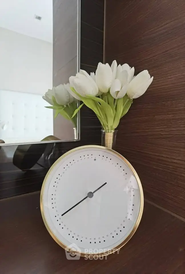 Elegant bedroom decor with modern clock and fresh tulips on wooden shelf.