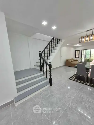 Modern open-plan living room with staircase and dining area, featuring sleek design and ample natural light.