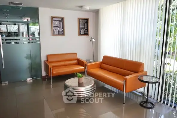 Modern lobby with orange sofas and glass accents in a bright, welcoming space.