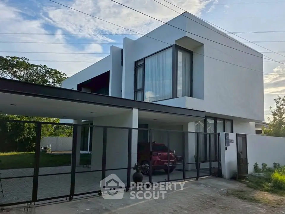 Modern minimalist house with sleek design and large windows, featuring a spacious carport and lush greenery.