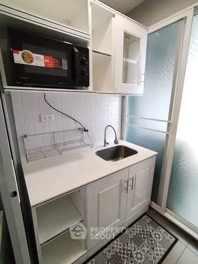 Compact modern kitchen with white cabinetry and built-in microwave, featuring a sleek sink and stylish backsplash.