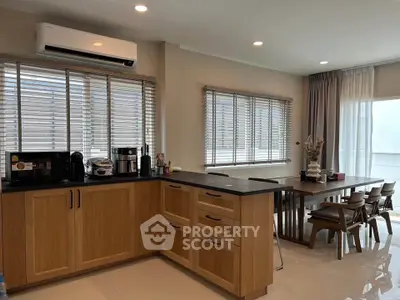 Modern kitchen with wooden cabinets and dining area, featuring natural light and sleek design.
