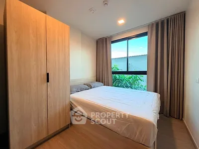Cozy bedroom with large window and wooden wardrobe, perfect for relaxation.