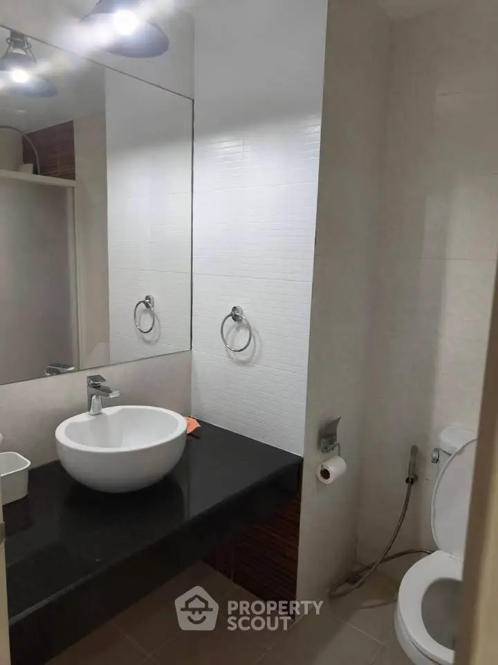 Modern bathroom with sleek black countertop and white basin, featuring a wall-mounted mirror and toilet.