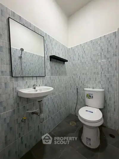 Modern bathroom with sleek tiles, wall-mounted sink, and efficient toilet design.