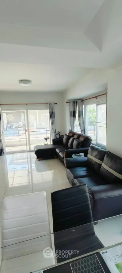 Spacious modern living room with sleek black sofas and large windows for natural light.