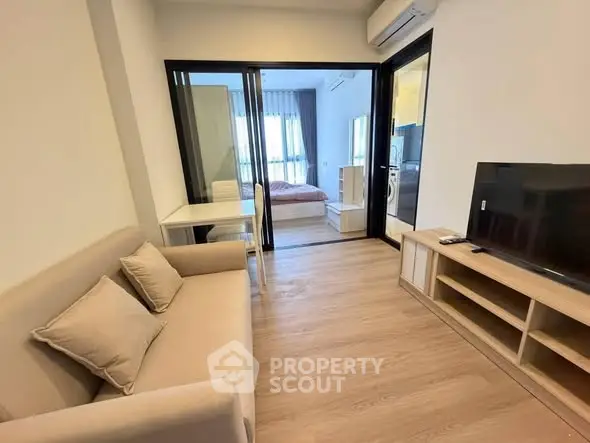 Modern living room with cozy sofa, TV, and view into bedroom, featuring sleek wooden flooring.