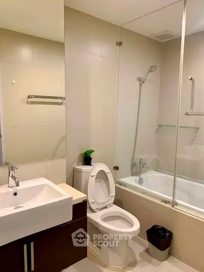 Modern bathroom with glass-enclosed bathtub and sleek fixtures in a contemporary apartment.