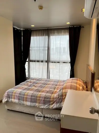 Cozy bedroom with large window and city view, featuring modern decor and ample natural light.