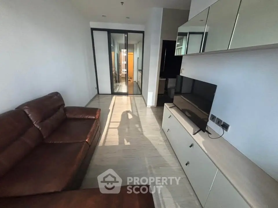 Modern living room with sleek leather sofa and wall-mounted TV unit, featuring a glass partition leading to other rooms.