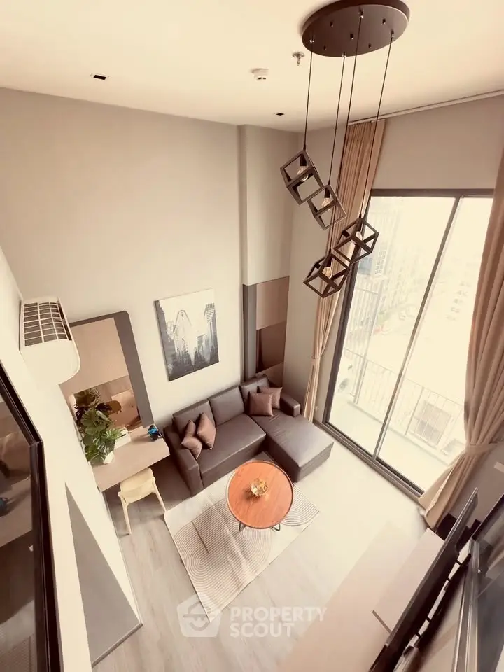 Modern living room with high ceiling and large windows offering city views.