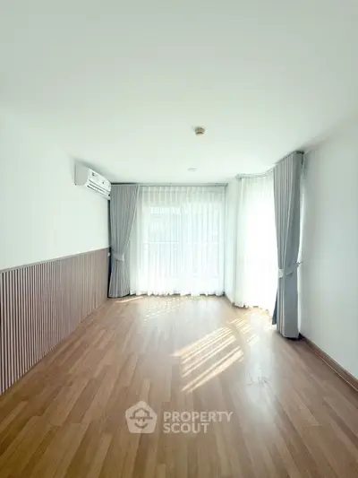 Spacious empty room with wooden flooring and large windows, perfect for customization.