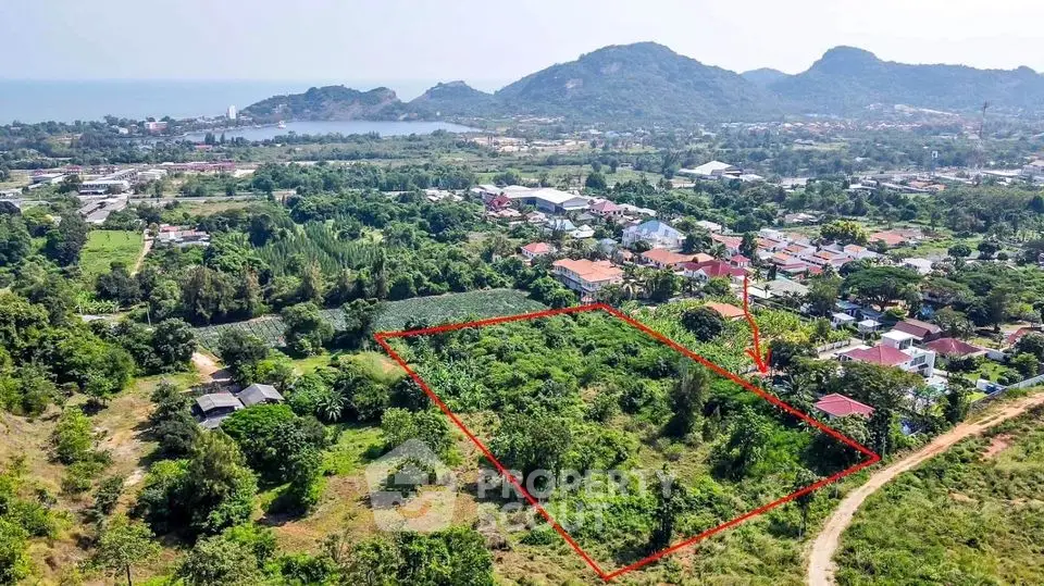 Expansive lush green land parcel available, outlined for clarity, with scenic mountain views and nearby community, ideal for development.