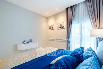 Elegant bedroom with modern decor and natural light, featuring plush blue bedding and stylish wall art.