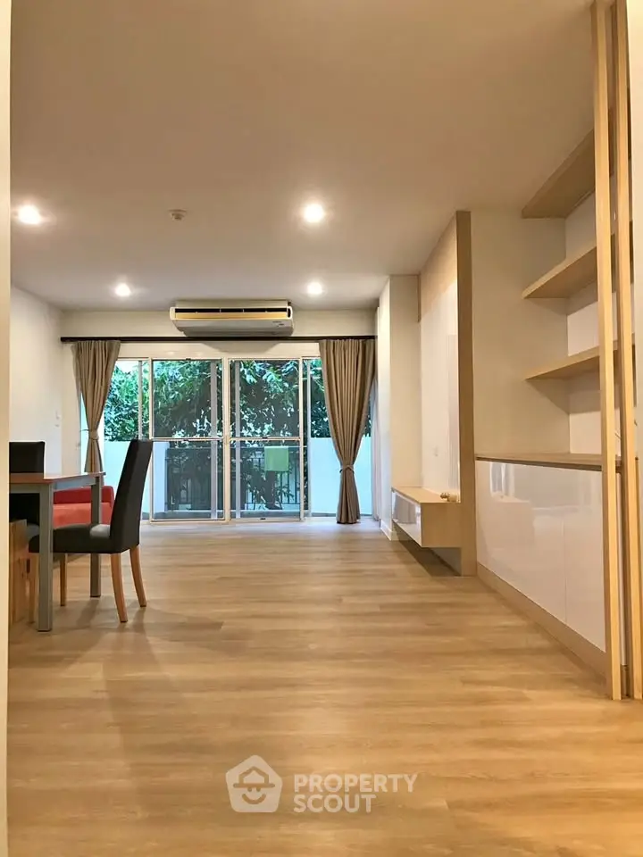 Spacious living room with wooden flooring and large windows offering natural light and garden view.