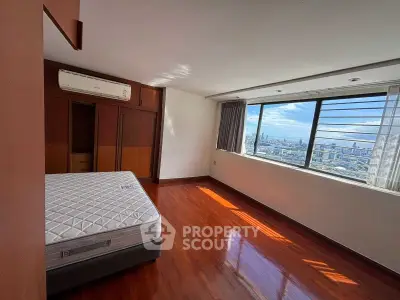 Spacious bedroom with stunning city view and wooden flooring in high-rise apartment.