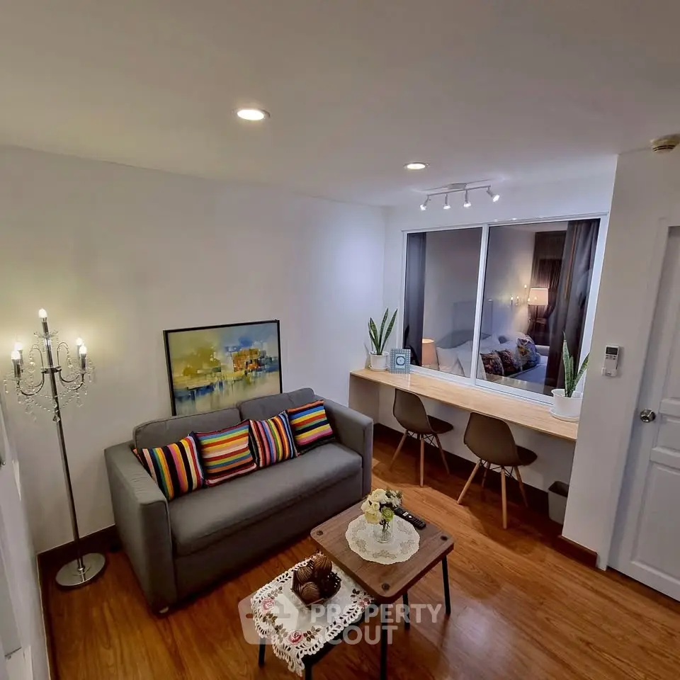 Modern living room with cozy seating and stylish decor, featuring a window view into a bedroom.